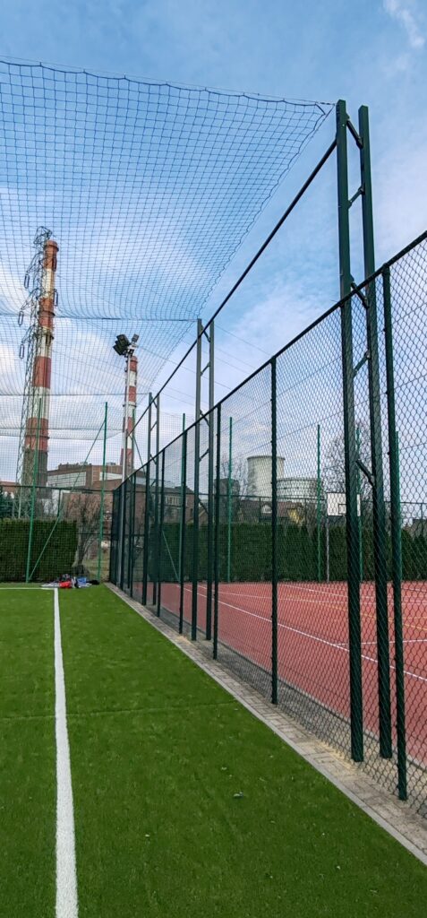 Siatka ochronna nad boiskiem sportowym. Konstrukcja zadaszenia ze wspornikami. Piłkochwyty. realizacja siatki ochronnej