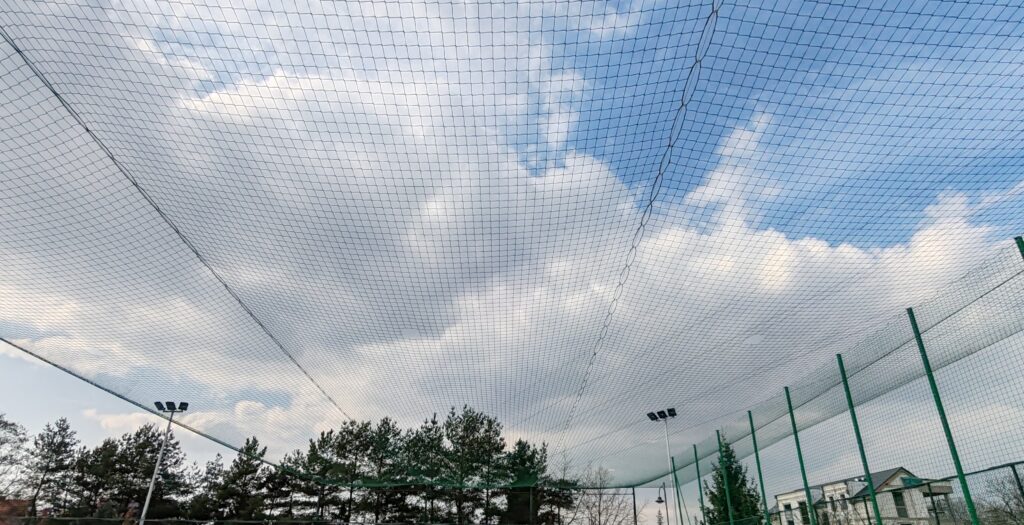 Siatka nad boiskiem, niebo w chmurach. Zadaszenie boiska sportowego z siatki polietylenowej. realizacja siatki ochronnej